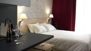 A hotel room with a bed, bedside lamps, a wooden table with a bottle and glasses, and a brick-patterned wall.
