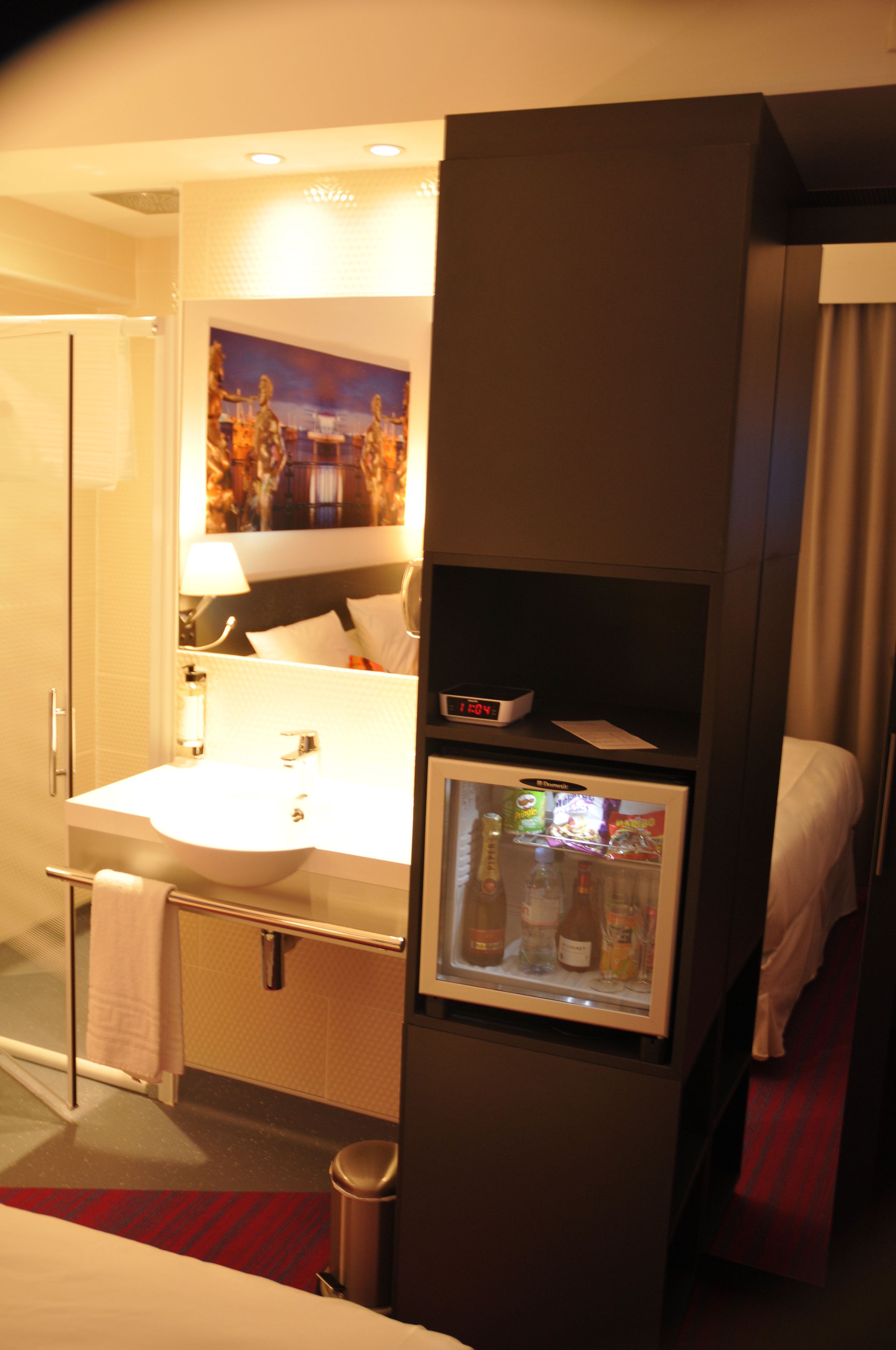 Ett hotellbadrum med handfat, spegel och ett litet kylskåp.