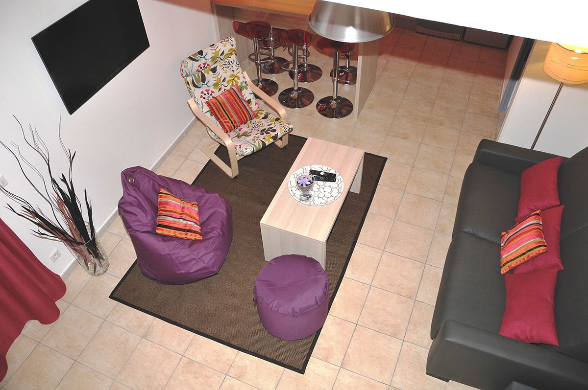Un salon comprenant un canapé, une table basse, un pouf violet, un fauteuil à motifs et un coin bar avec des tabourets.
