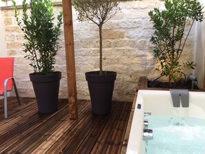 A wooden deck with potted plants, a stone wall, and a spa tub. - Privilège Hôtel & Apparts Eurociel Centre Comédie (Montpellier)
