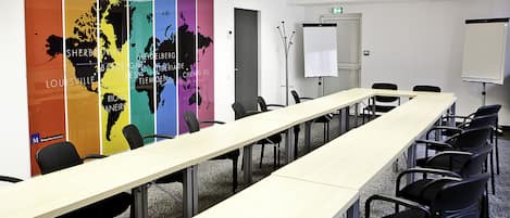 Un salón de conferencias con una larga mesa, sillas, una pizarra y coloridos mapas mundiales en la pared.