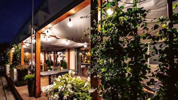 An outdoor dining area with tables and chairs, a covered seating area, and potted plants. - Arche Hotel Puławska Residence (Warsaw)