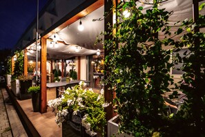 An outdoor dining area with tables and chairs, a covered seating area, and potted plants. - Arche Hotel Puławska Residence (Warsaw)