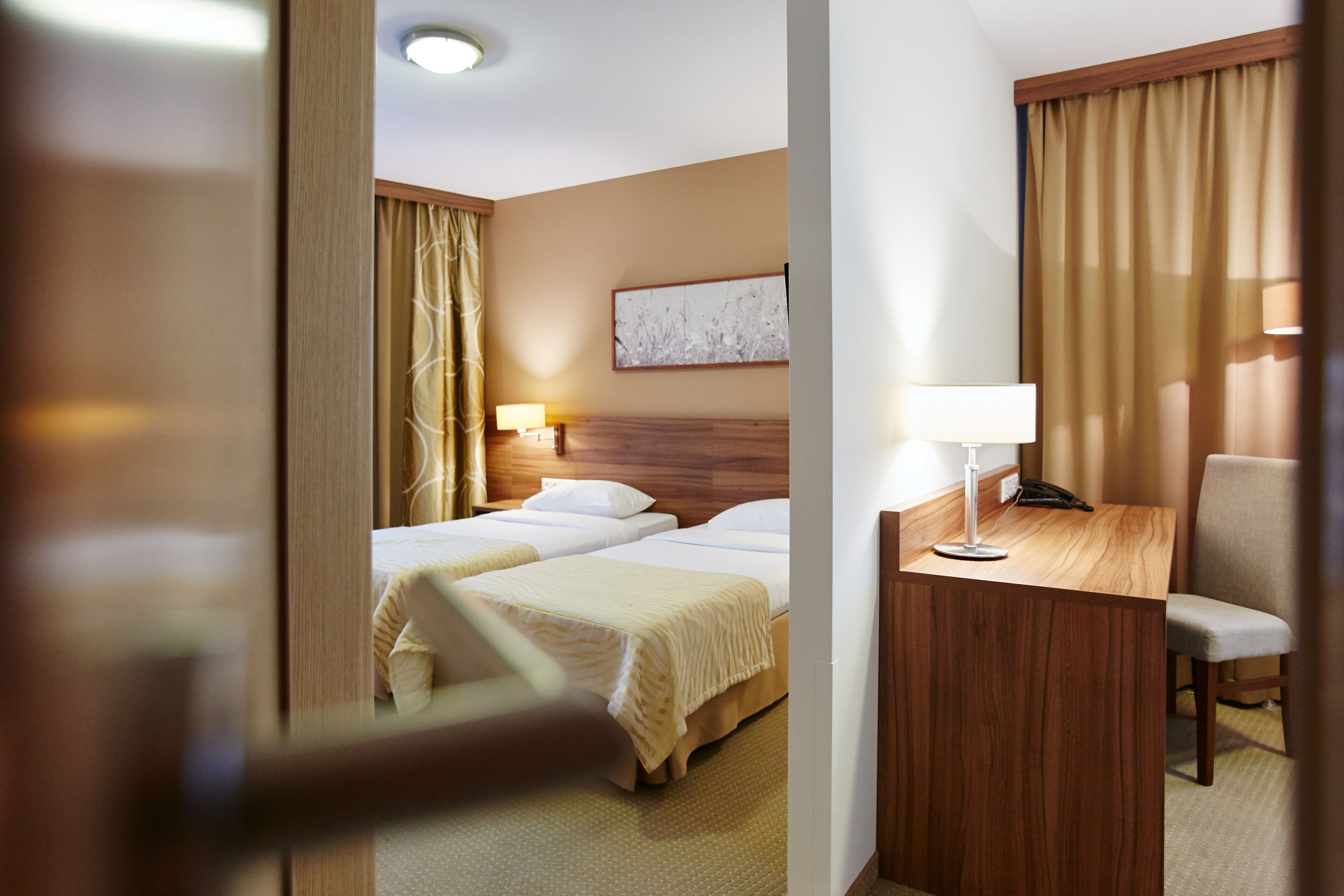 Una habitació d'hotel amb dos llits, un escriptori amb una làmpada, una cadira i un quadre a la paret.