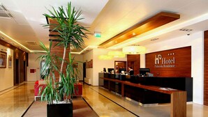 A modern hotel lobby with a reception desk, a large potted plant, and a polished floor. - Arche Hotel Puławska Residence (Warsaw)