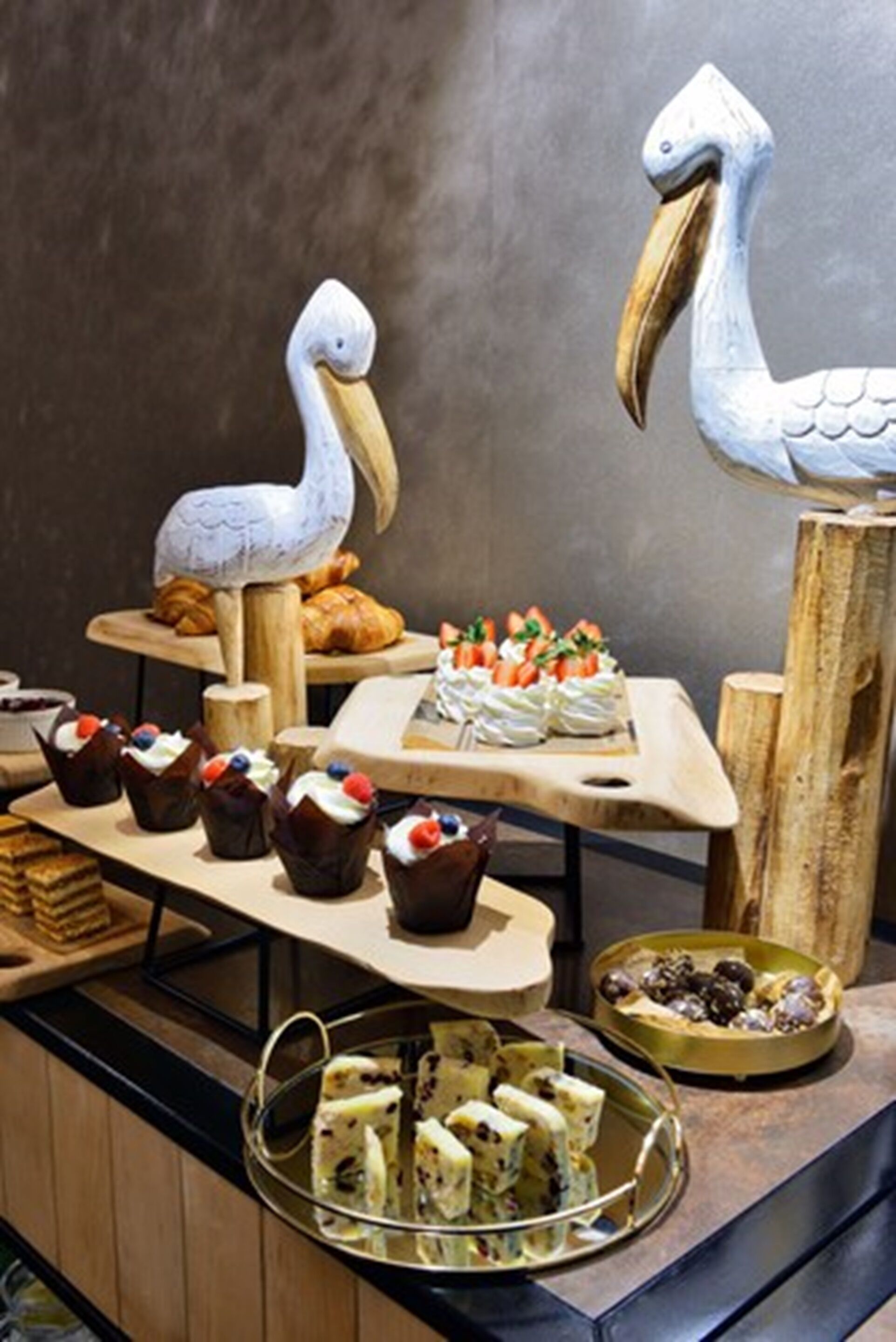 A buffet with various food items including cupcakes, pastries, and a tray of sandwiches.