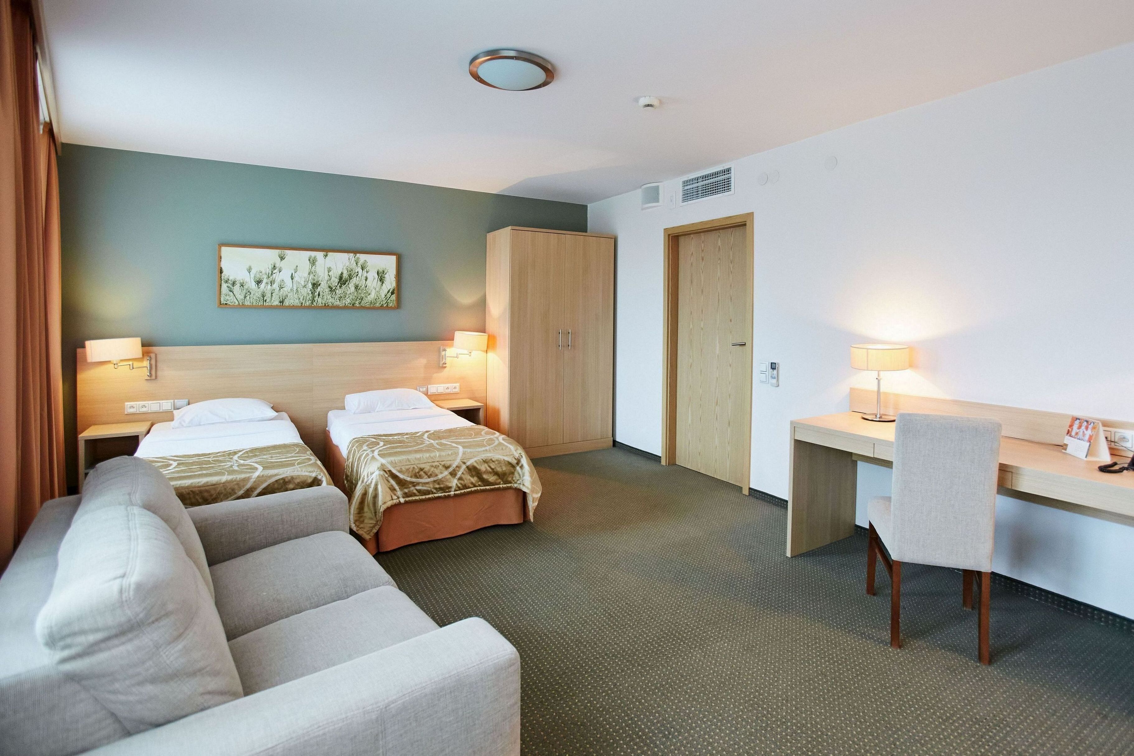 A hotel room with two beds, a desk, a chair, and a wardrobe.