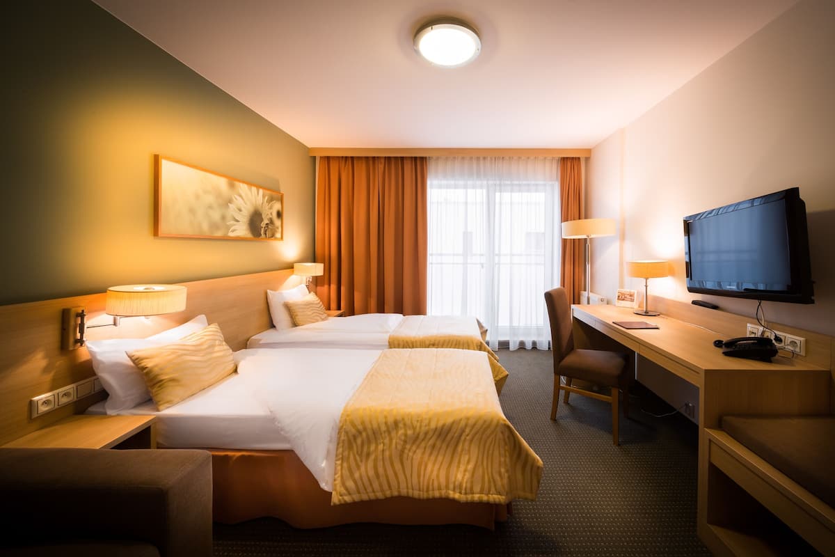 A hotel room with two beds, a desk, a chair, a television, and a window with curtains.