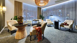 A modern hotel lobby with a round table, several armchairs, a large vase, and a decorative ceiling light. - Arche Hotel Puławska Residence (Warsaw)