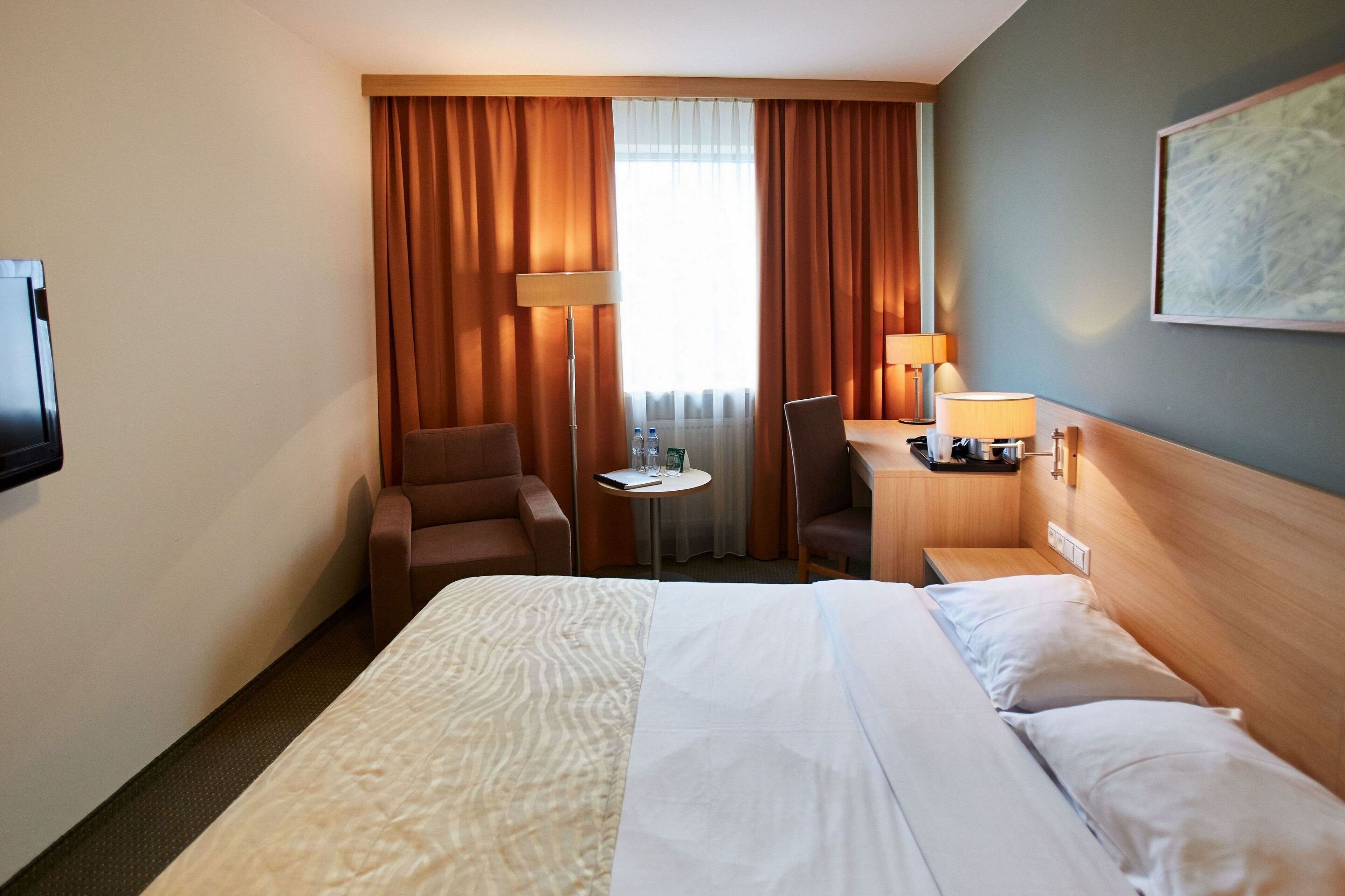Ein Hotelzimmer mit einem Bett, zwei Sesseln, einem kleinen Tisch, einer Lampe und einem Bild an der Wand.