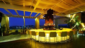 A bar area with a central pillar, multiple bar stools, and a view of the city at night. - Daspalla Hyderabad (Hyderabad)