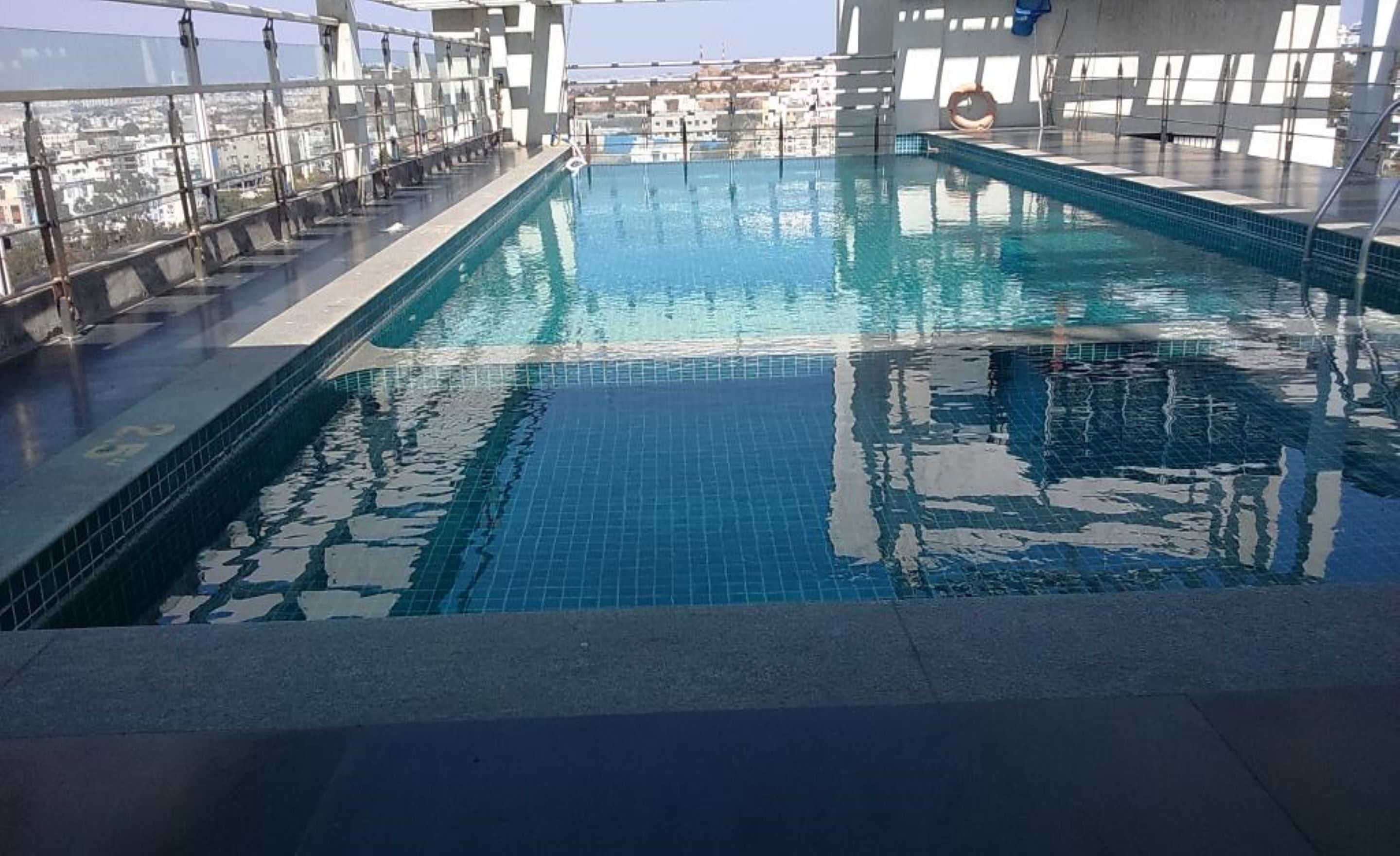 Une piscine intérieure à l’eau d’un bleu cristallin, entourée d’une balustrade en verre et offrant une vue sur le paysage urbain.