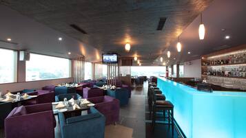 A modern restaurant with a bar area, featuring a mix of seating options and a view of the city.