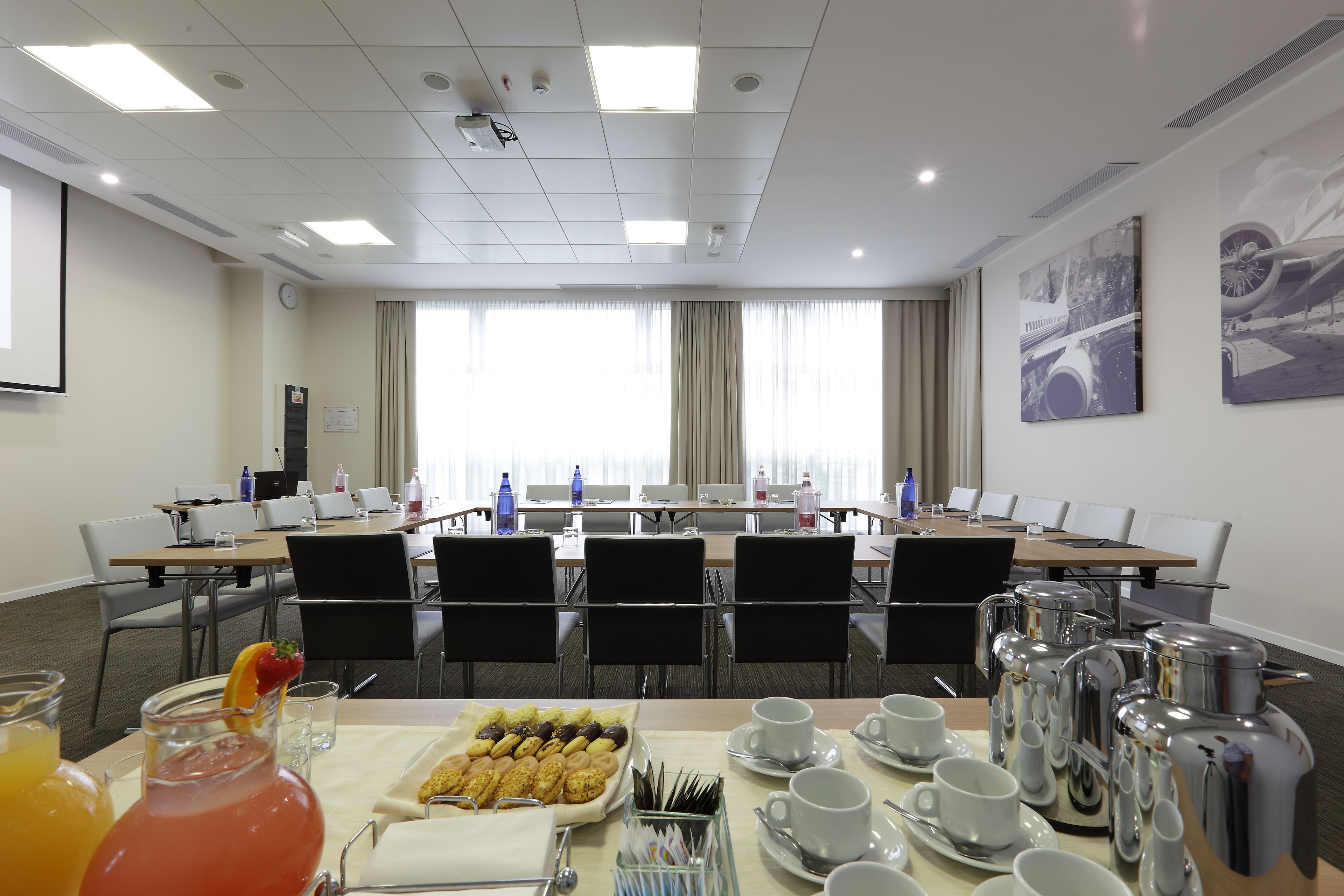 Een vergaderruimte met een lange tafel, stoelen, een beamer en een buffet met eten en drinken.