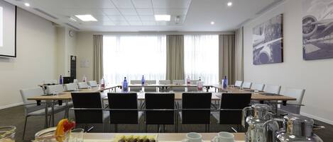 Un salón de conferencias con una larga mesa, sillas, un proyector y un bufé con comida y bebidas.