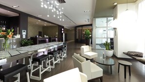 Un moderno hall de hotel con mostrador de recepción, zona de bar, asientos y una gran planta en maceta.