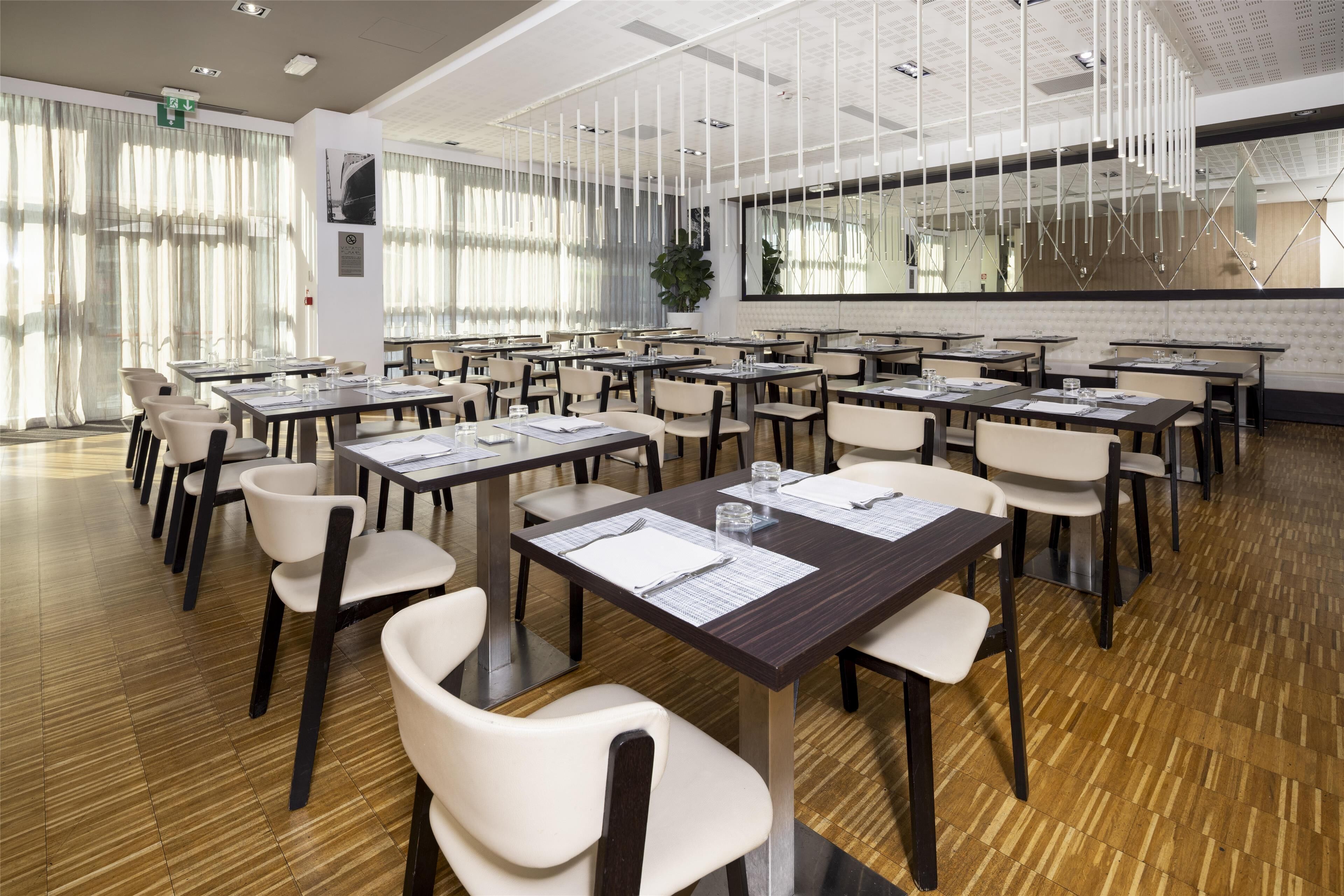 A conference room with multiple tables and chairs, large windows with sheer curtains, and a modern ceiling design.
