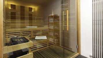 Un espai de sauna amb seients de fusta, una porta de vidre i un radiador metàl·lic.