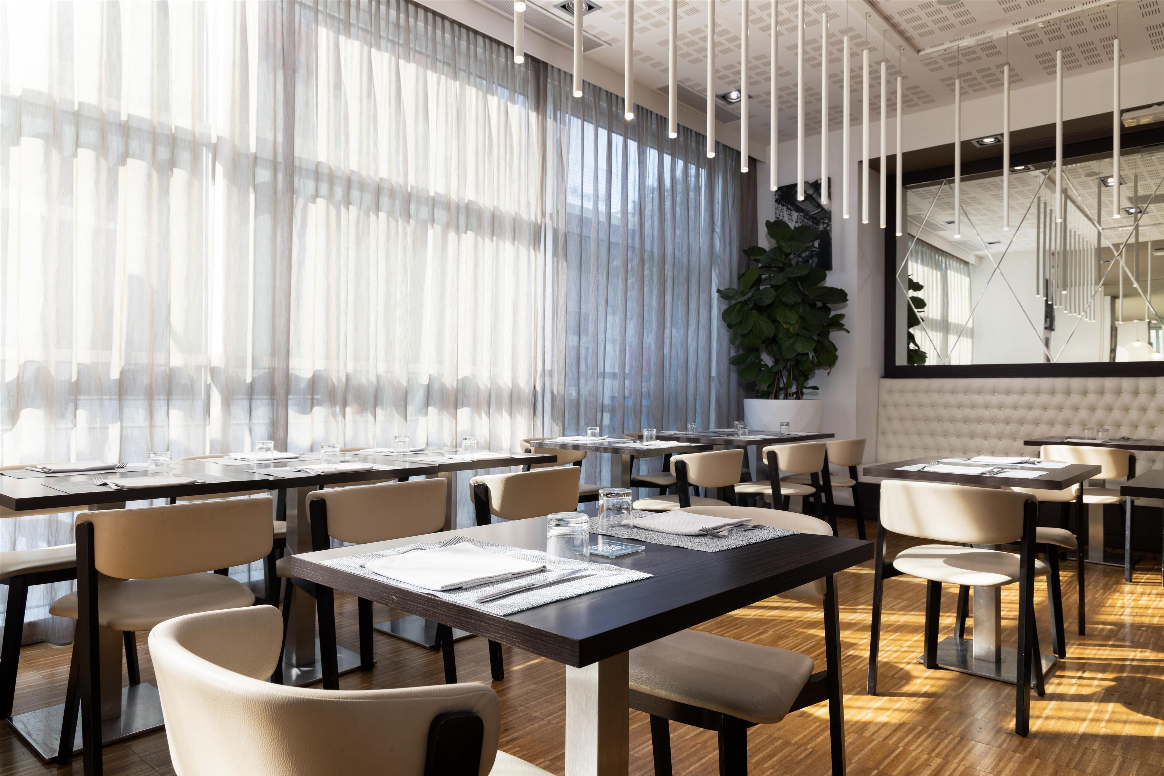 A modern dining area with tables set for two, featuring a clean, minimalist design with light-colored chairs and dark tables.