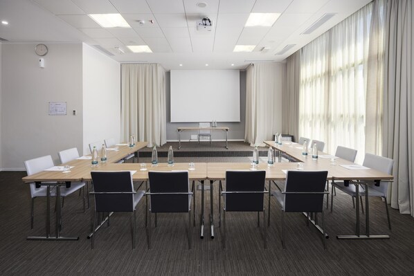 Un salón de conferencias con una larga mesa, sillas, una pantalla de proyector y un reloj en la pared.