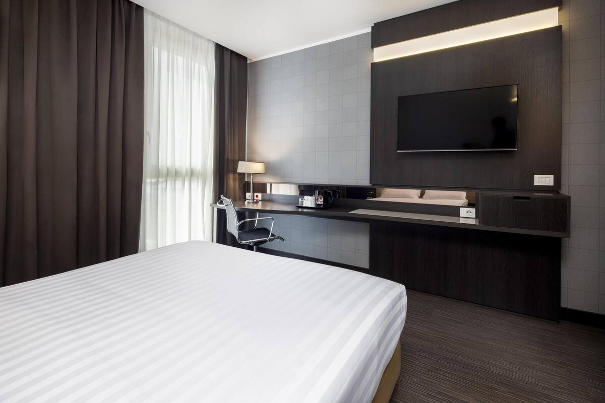 Een moderne hotelkamer met een groot bed, een bureau met stoel, een flatscreen televisie aan de muur en een raam met gordijnen.