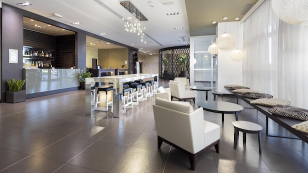 Un moderno vestíbulo de hotel con área de bar, espacios de descanso y un mostrador de recepción.