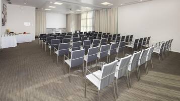 Un salón de conferencias con filas de sillas, una pantalla de proyector y una mesa con refrigerios.