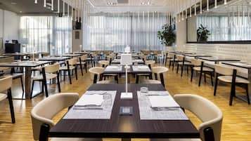 Un'ampia sala da pranzo con diversi tavoli e sedie, grandi finestre con tende leggere e un moderno design del soffitto.