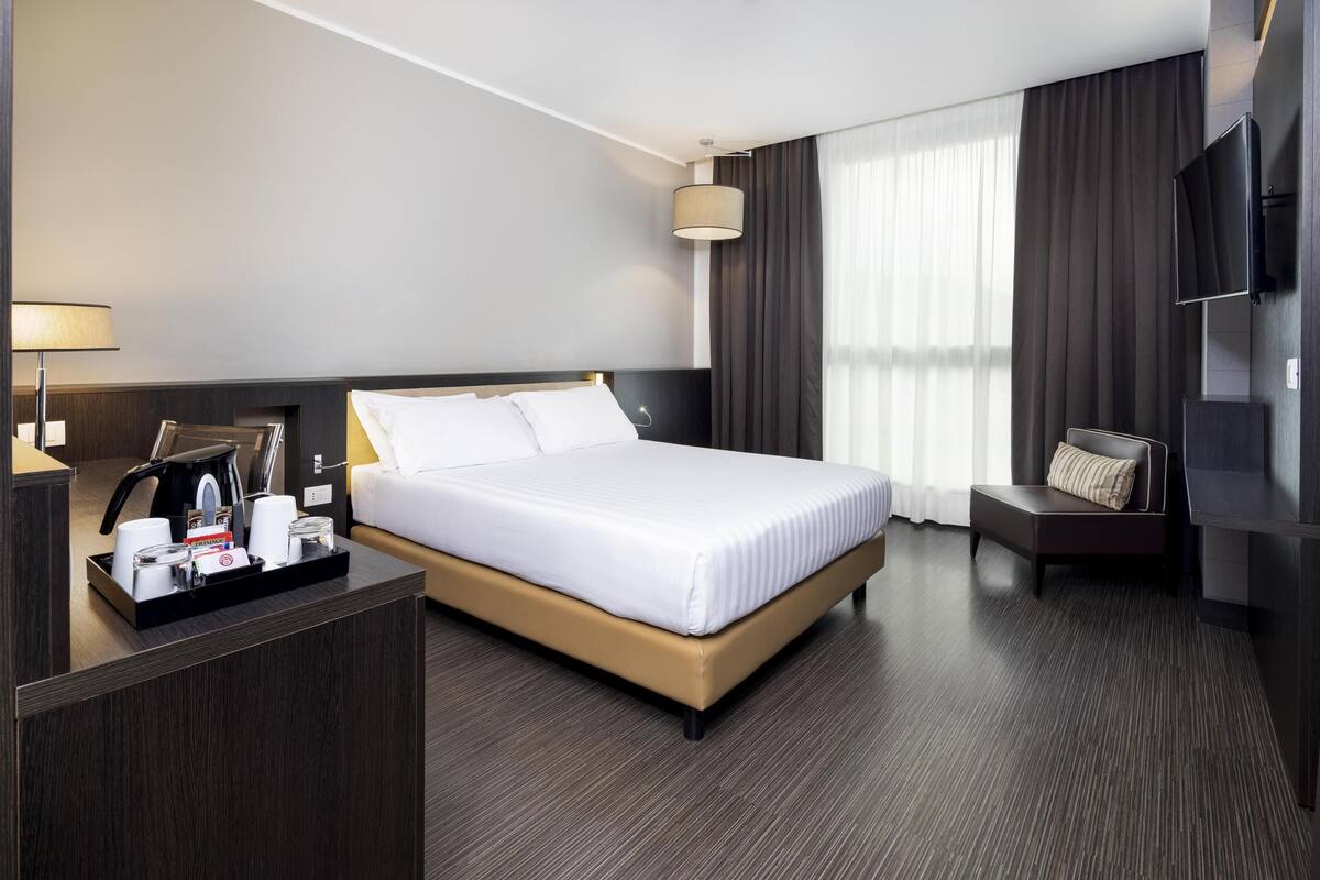 Een moderne hotelkamer met een groot bed, een nachtkastje met een lamp, een televisie en een zithoek.