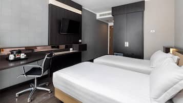 Ein modernes Hotelzimmer mit Schreibtisch, zwei Betten, Fernseher und Kleiderschrank.