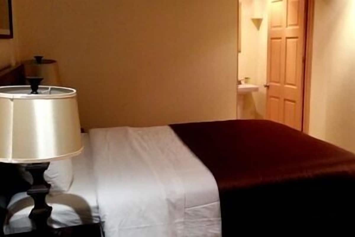 A hotel room with a bed, a bedside lamp, a TV mounted on the wall, and a door leading to the bathroom.