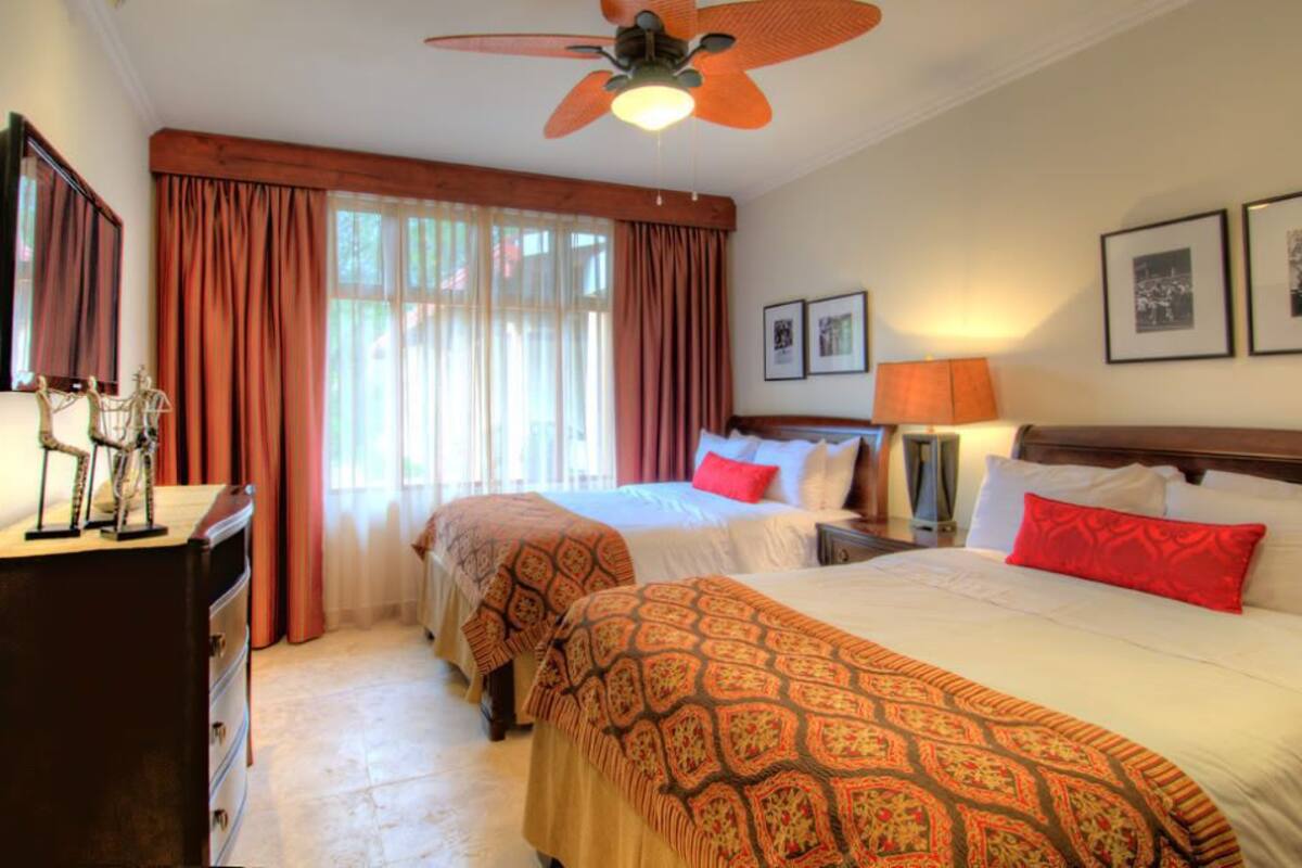 A hotel room with two beds, a ceiling fan, a dresser, and a window with curtains.