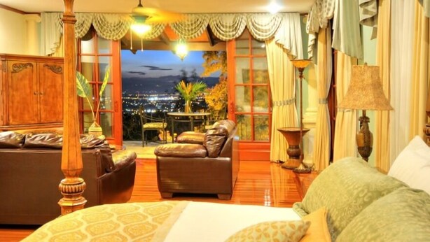 A bedroom with a four-poster bed, a sofa, a small table, and a view of a cityscape at night. - Ringle Resort & Spa (Escazu)