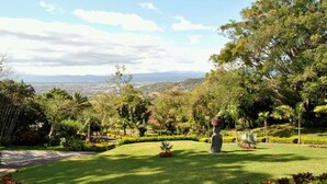 A landscaped garden with a statue, lush greenery, and a view of distant hills. - Ringle Resort & Spa (Escazu)