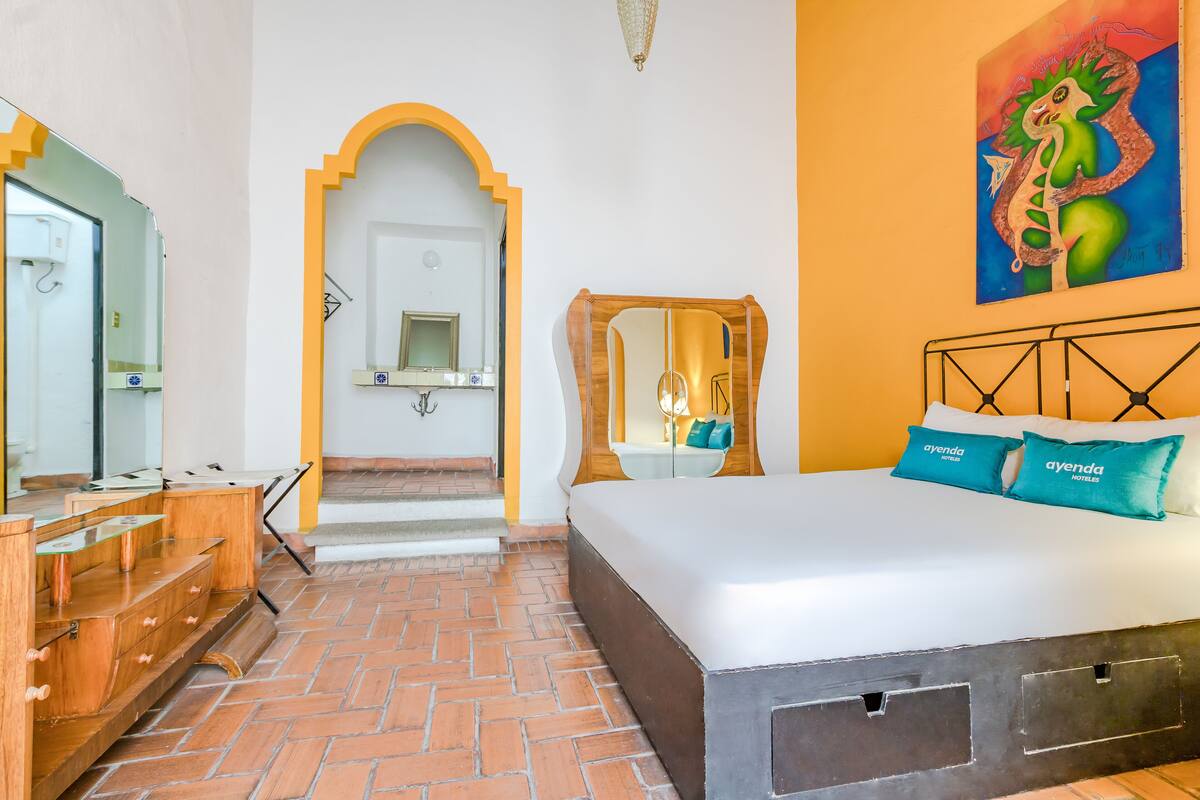 Een hotelkamer met een bed, een houten dressoir, een spiegel en een schilderij aan de muur.