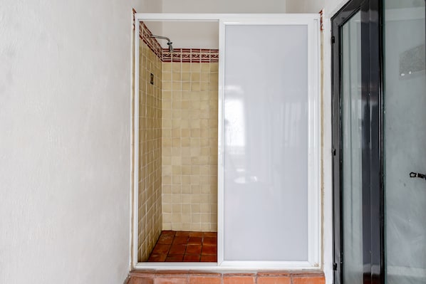 A bathroom with a tiled shower area and a door leading to a room.