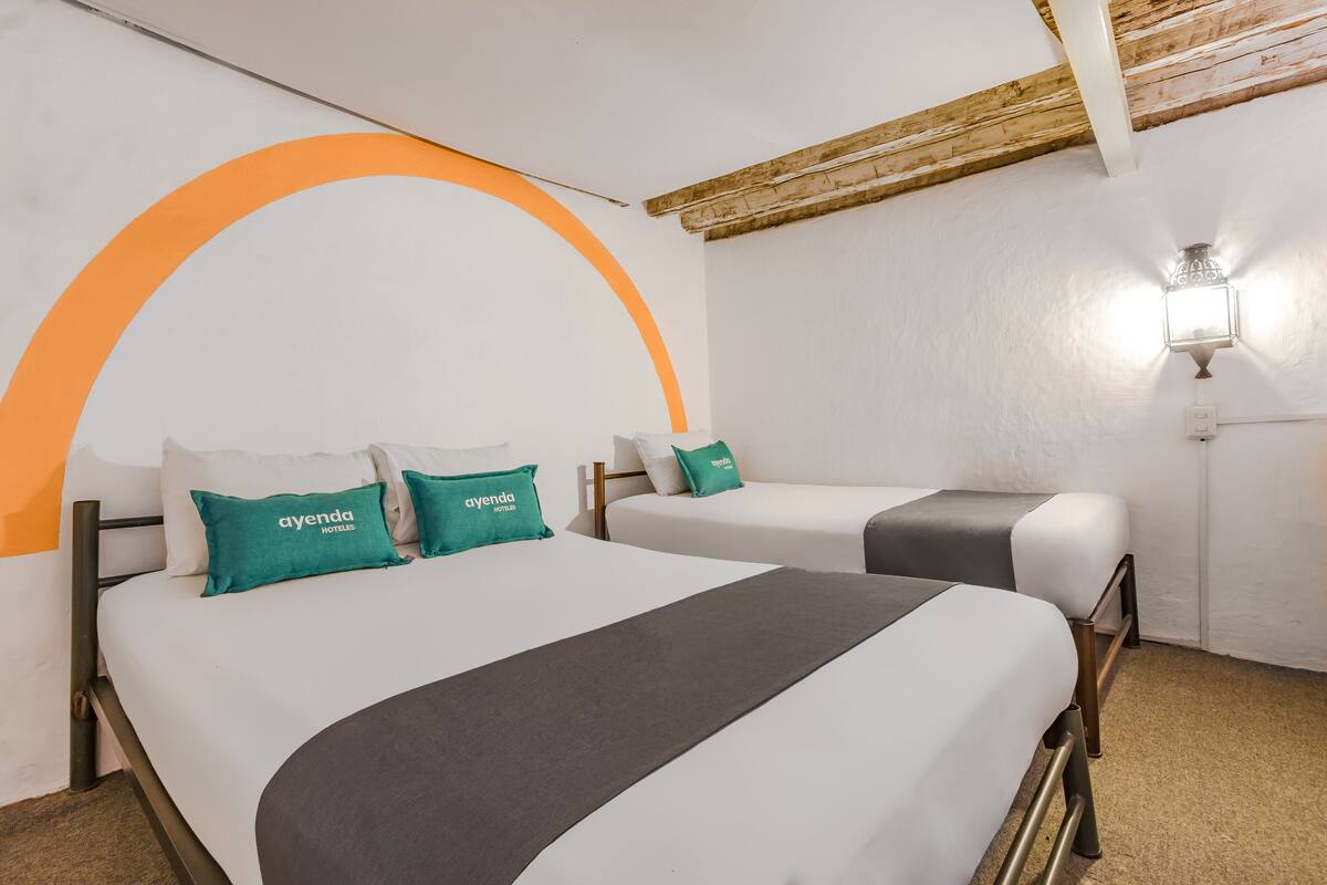 Een hotelkamer met twee bedden, elk met een witte matras en teal-kleurige kussens met de tekst 'ayenda HOTEL'.