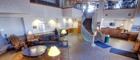 A spacious lobby with a stone floor, leather seating, a wooden coffee table, and a staircase leading to an upper level.