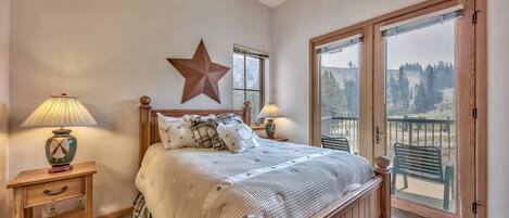 Quarto com uma cama grande, duas luminárias de cabeceira, um adorno em formato de estrela e uma varanda com vista para árvores.