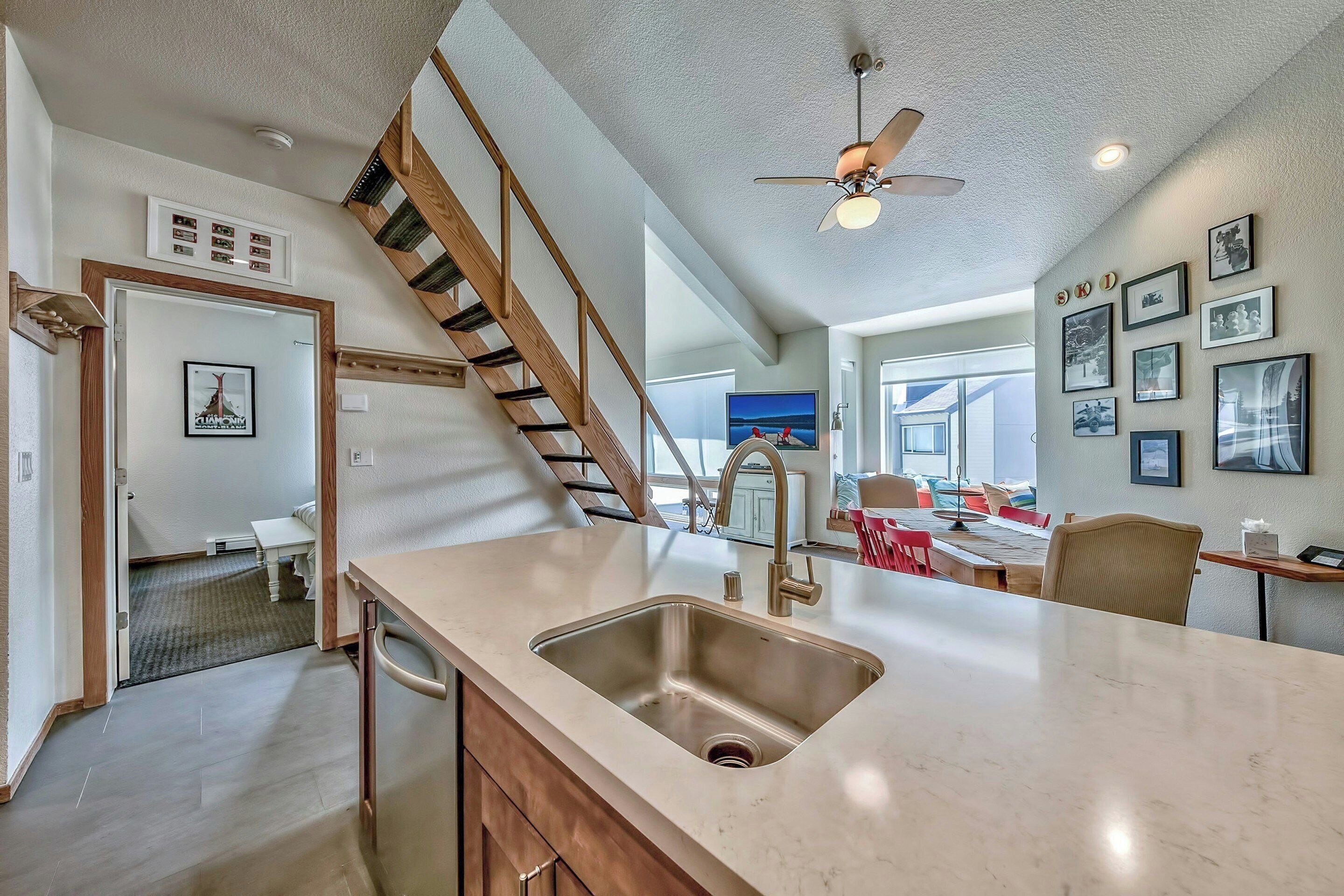 A kitchen with a stainless steel sink, wooden cabinets, a staircase, and a dining area with a table and chairs.