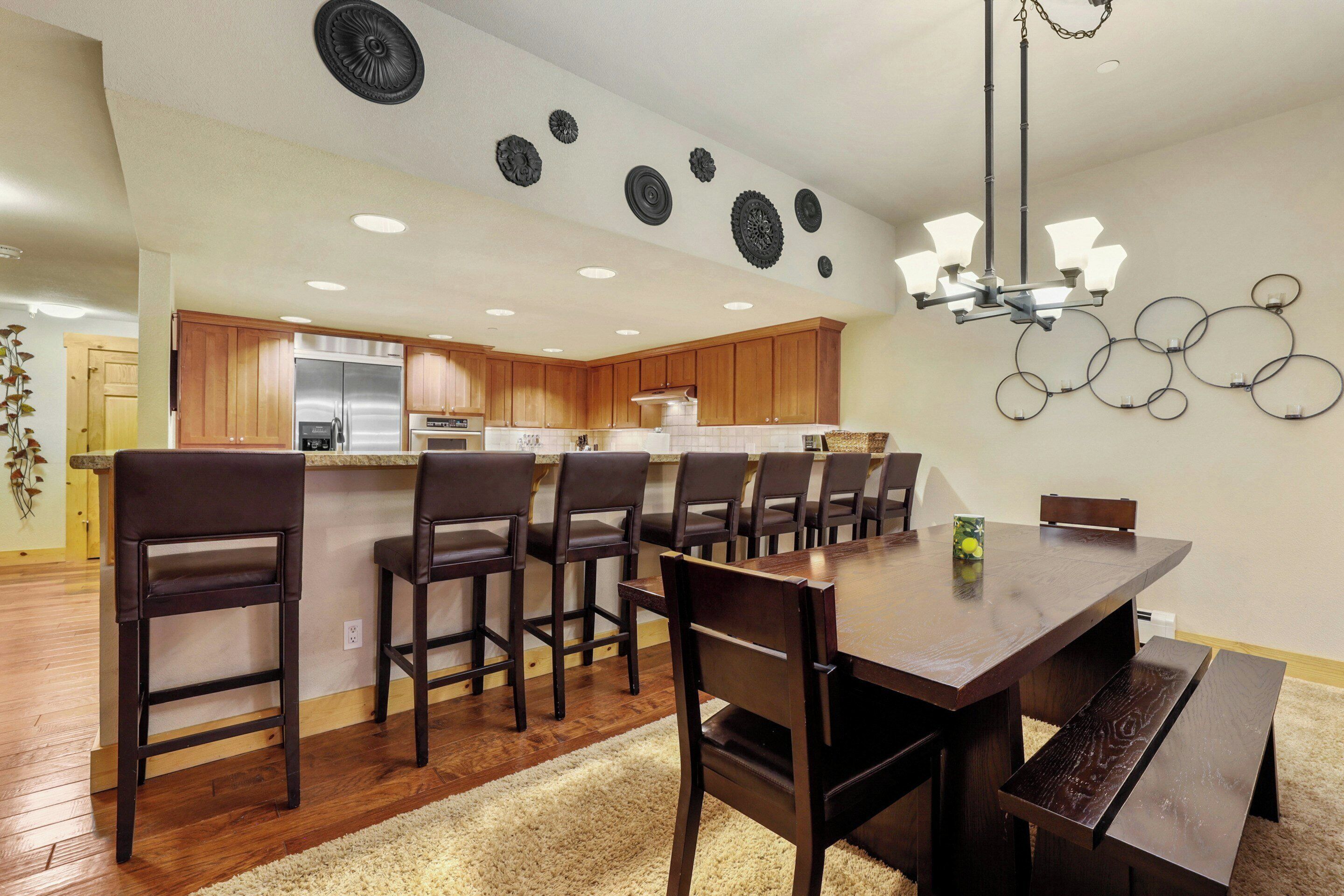 A modern kitchen with wooden cabinets, a stainless steel refrigerator, and a dining area with a large wooden table and chairs.