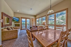 A spacious living room with a wooden dining table and chairs, a large mirror, and a television.