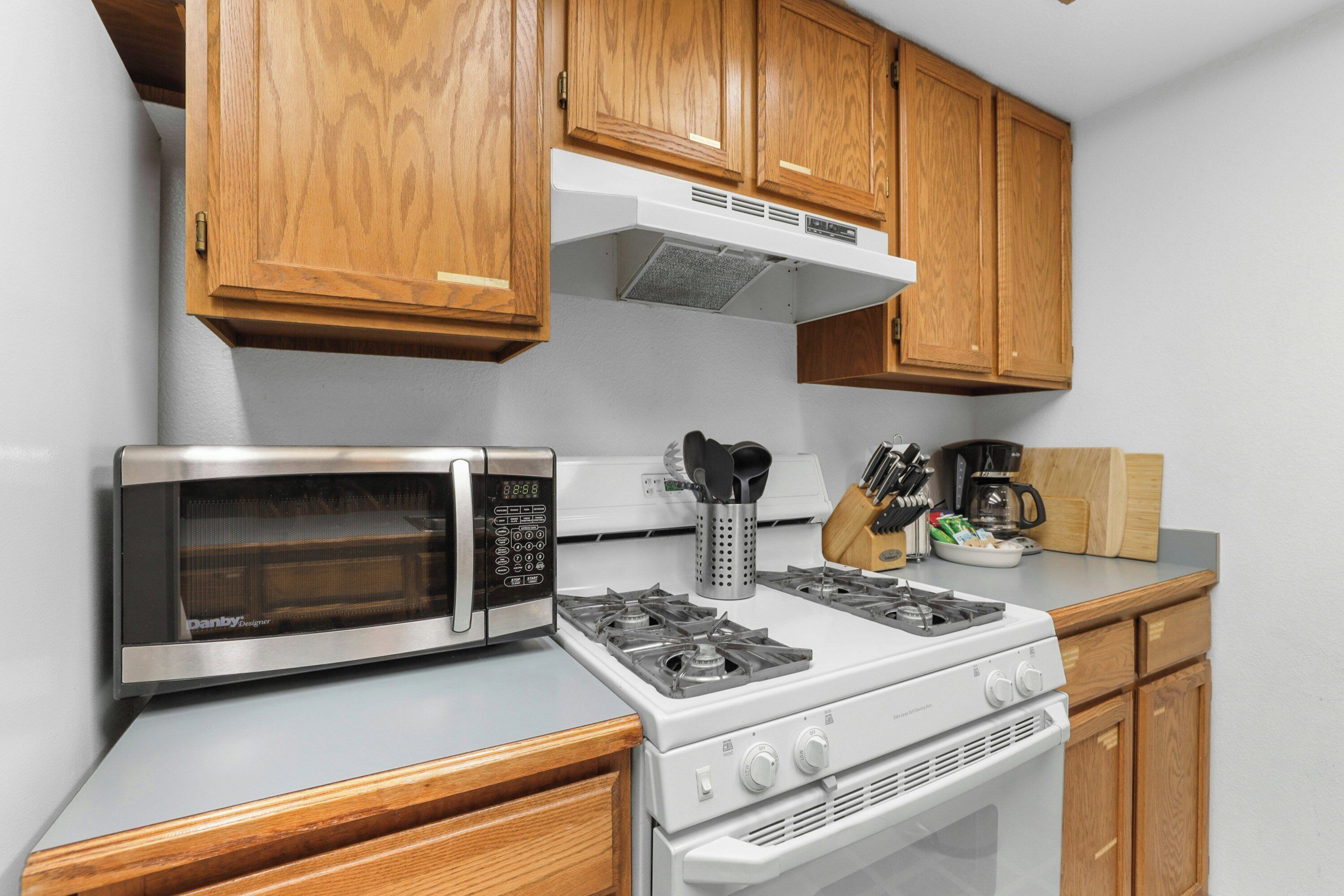 A kitchen with wooden cabinets, a stainless steel microwave, a gas stove, and a coffee maker.