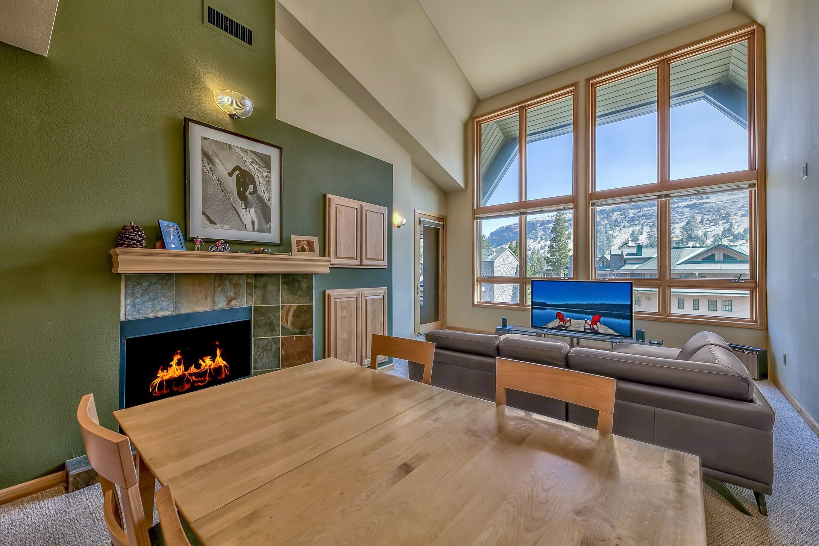 A living room with a fireplace, a large window with a view, a dining table, and a sofa.