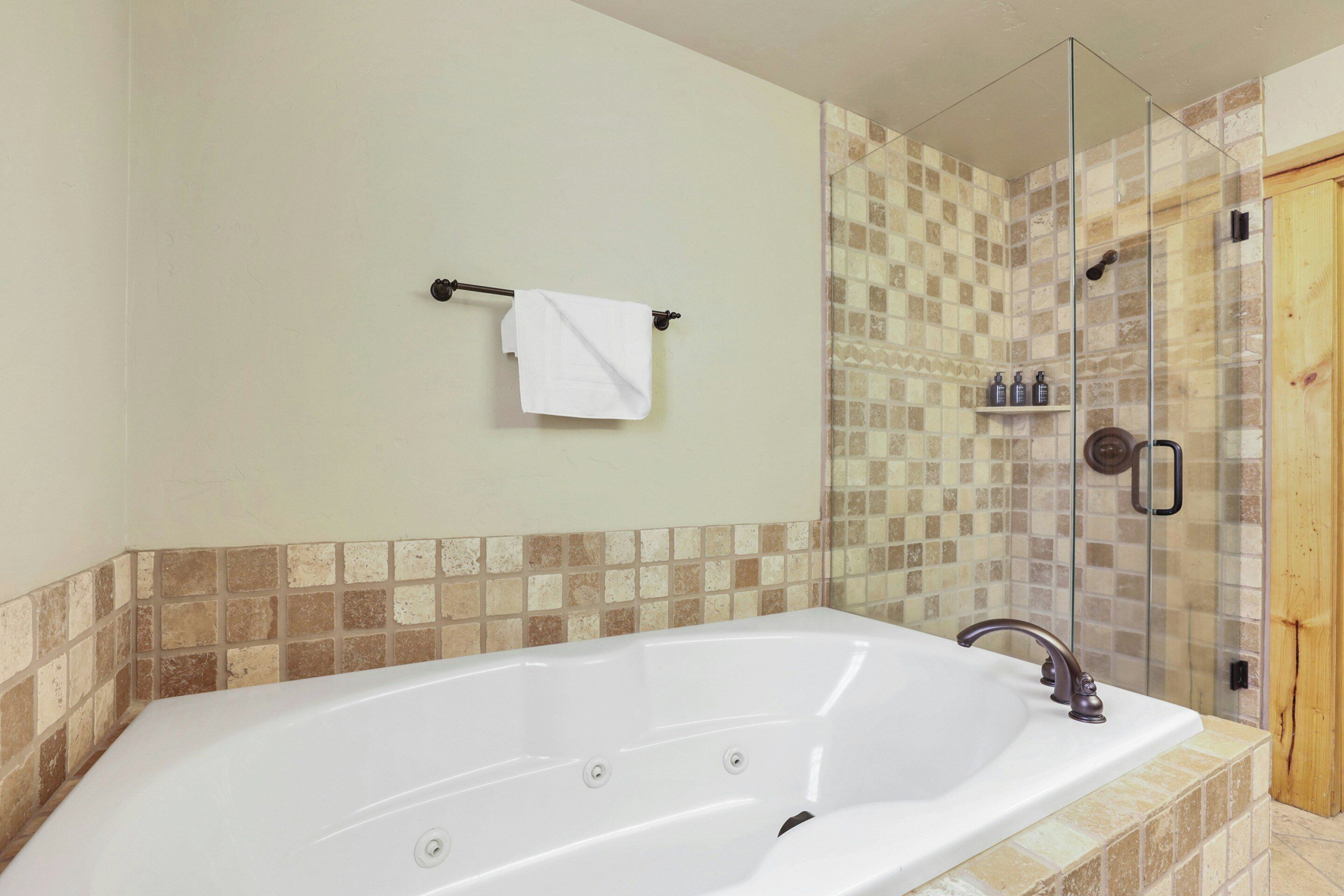 A bathroom with a large white bathtub, a glass-enclosed shower, and a wooden door.