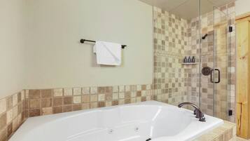 A bathroom with a large white bathtub, a glass-enclosed shower, and a wooden door.