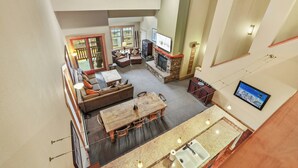A spacious living area with a high ceiling, a fireplace, a dining table, and a kitchen with a sink and countertop. - Kirkwood Mountain Resort by Vail Resorts (Kirkwood)