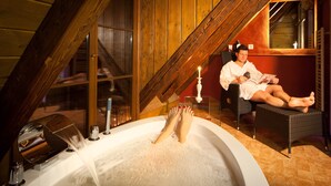 A person relaxing in a bathtub with a wooden ceiling and a window in the background.