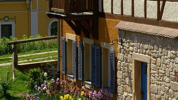 A traditional half-timbered building with a stone facade, a wooden balcony, and a flower garden in front.