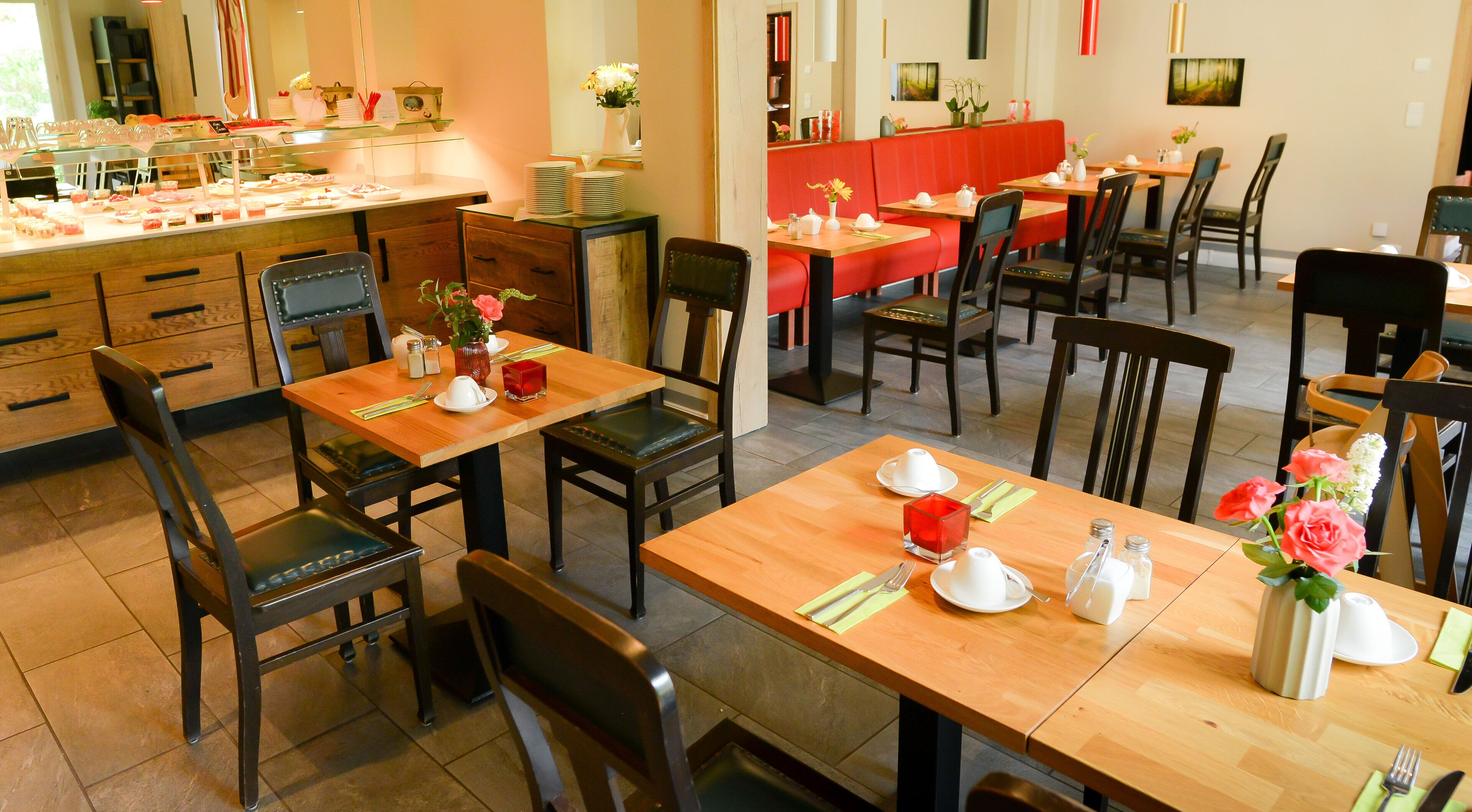 A restaurant with wooden tables and chairs, some with red cushions. There are flower vases on the tables.